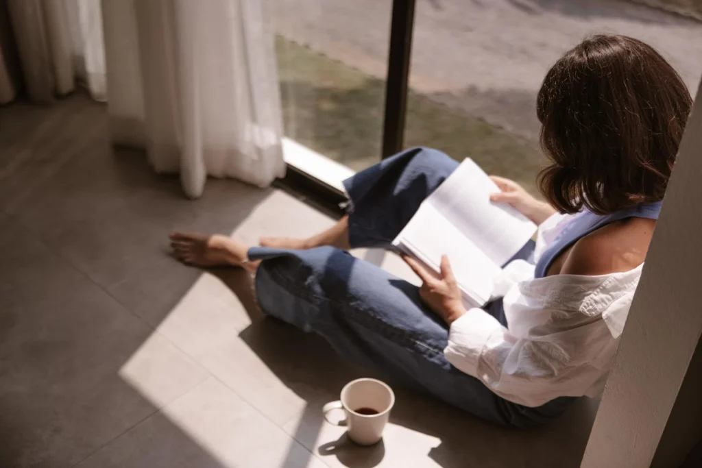 Mulher sentada no chão lendo um livro com luz natural — autoconhecimento e desenvolvimento pessoal no dia a dia